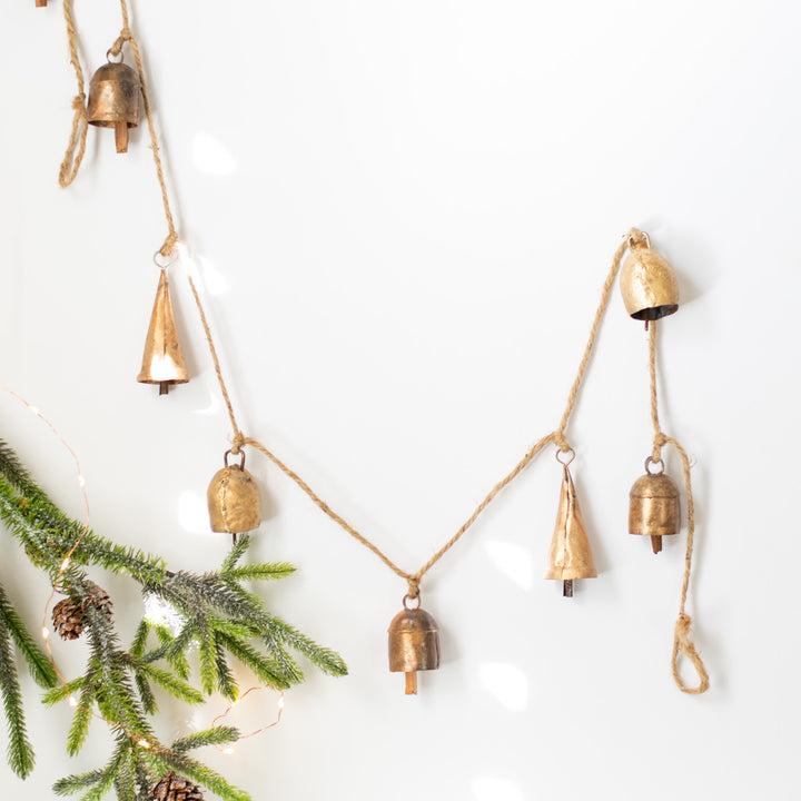 A close-up of a garland with gold bells hanging on a way next to a pine branch