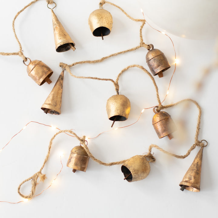 A close-up of a garland with gold bells scattered across a white background with a string light