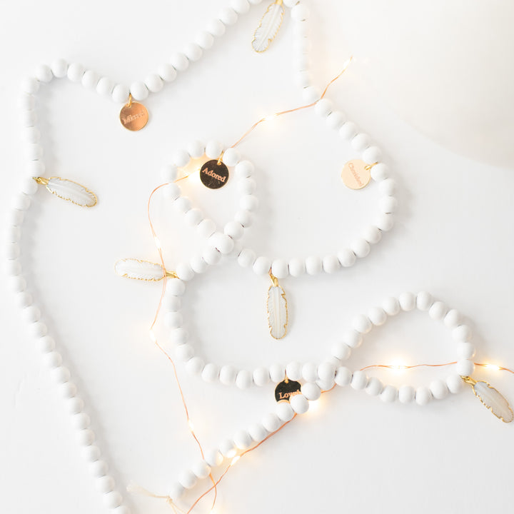 A close-up of a white garland with white feather charms and engraved gold charms against a white background