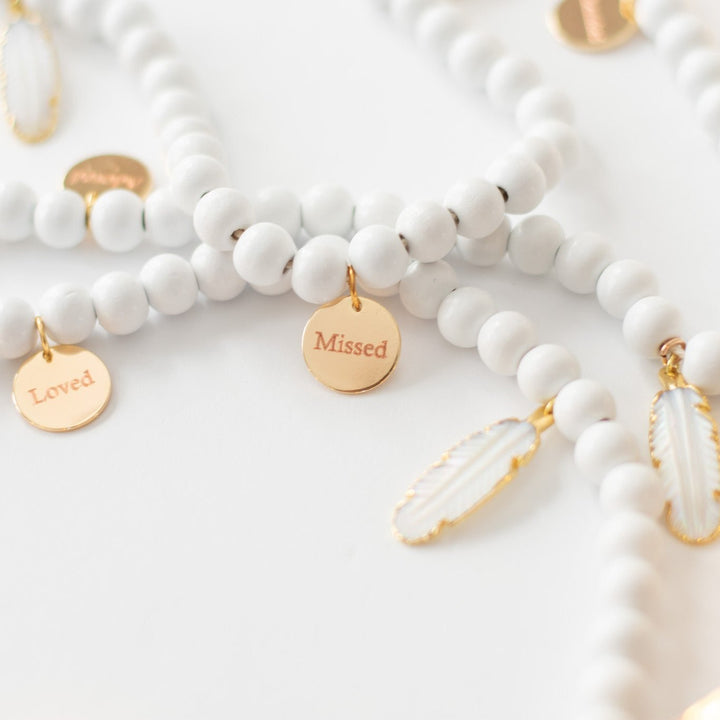 A close-up of a white garland with white feather charms and engraved gold charms against a white background