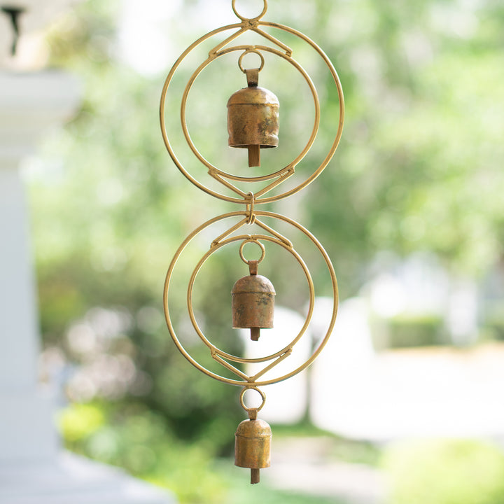 Close-up of a rustic wind chime of recycled tin and iron coated in copper showcasing three bells with a blurred background of a backyard