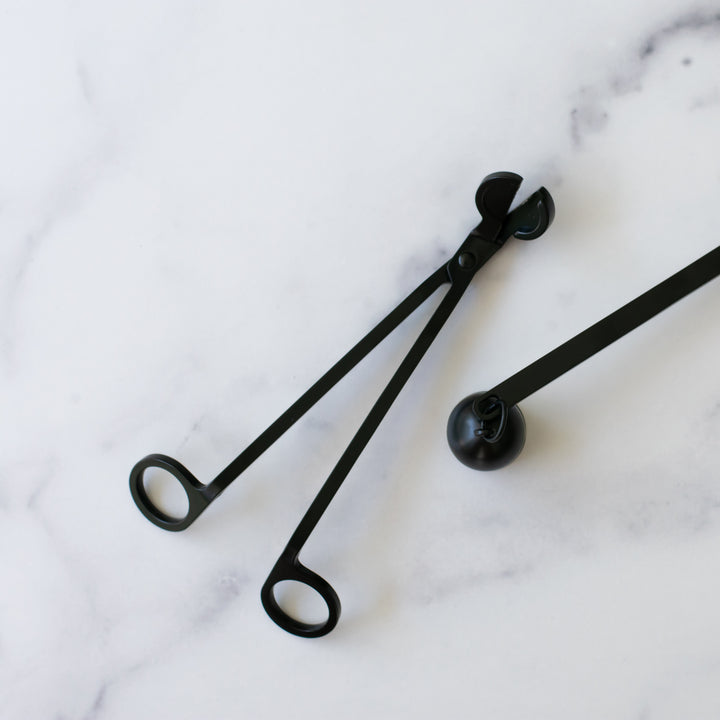 A close-up of black wick trimmer and black candle snuffer against a white background