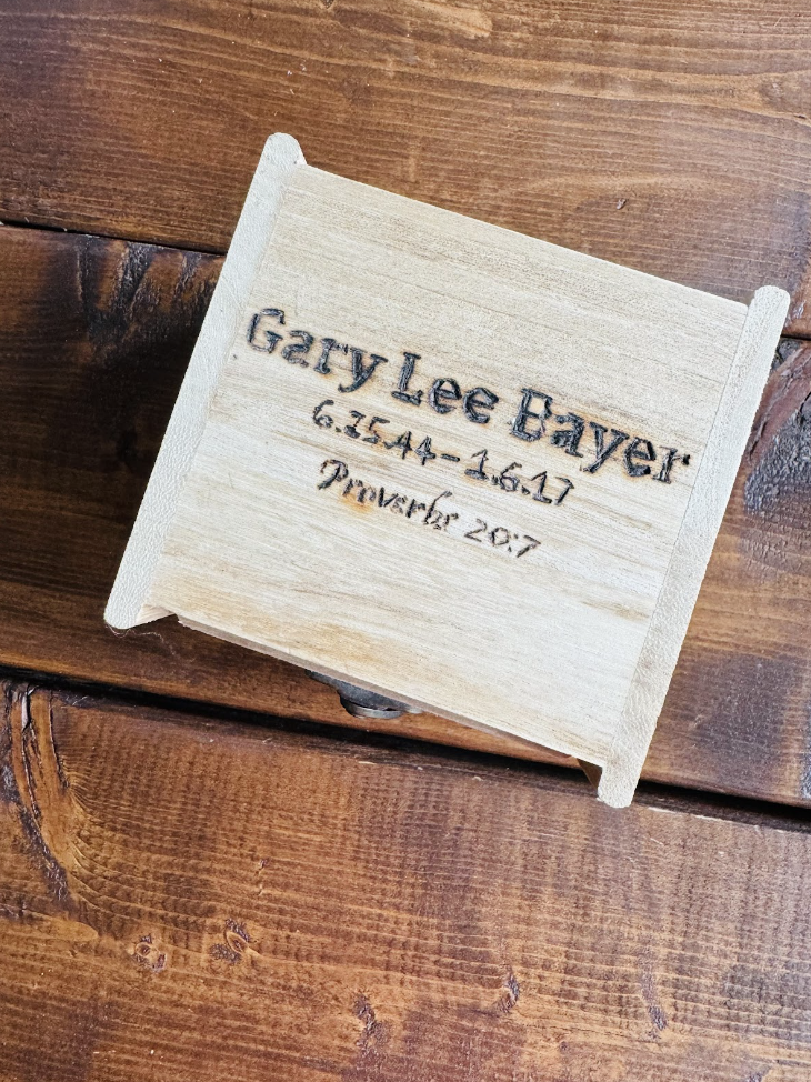 photo of a wooden box with the words "Gary Lee Bayer 6.25.44 - 1.6.17 Proverbs 20:7" branded into the top of the box