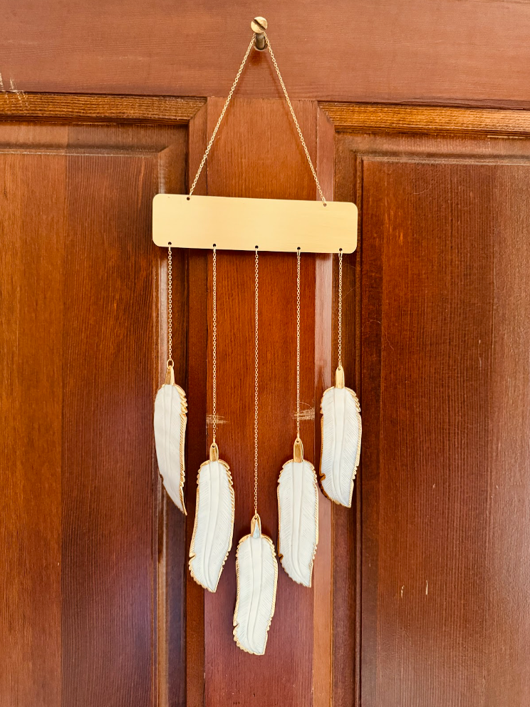 photo of gold wind chimes with white feathers as the chimes