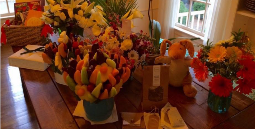 photo of edible arrangements, vases of flowers, gift baskets, stuffed animals and other gifts sitting on a table