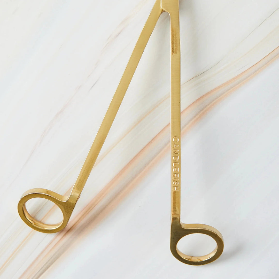A close-up of gold wick trimmers prongs against a white background