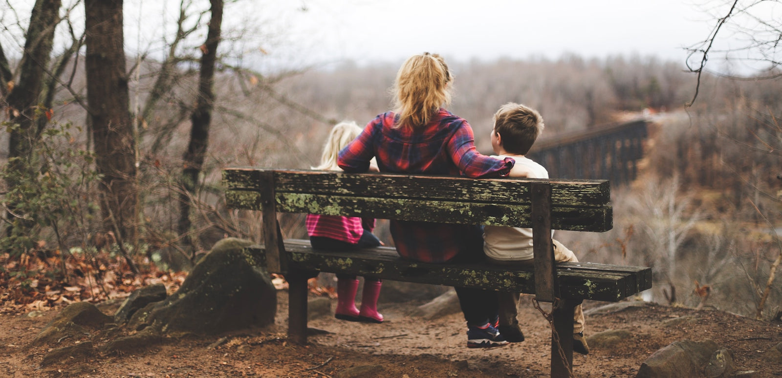 photo of a woman sitting with a young boy and young girl on either side of a bench looking out over a valley