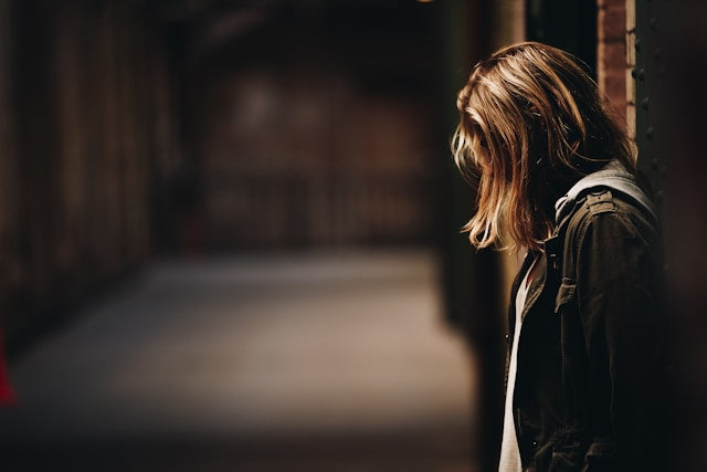 photo a a blonde woman standing in a dark brick alley with her hair covering her face as she look downward