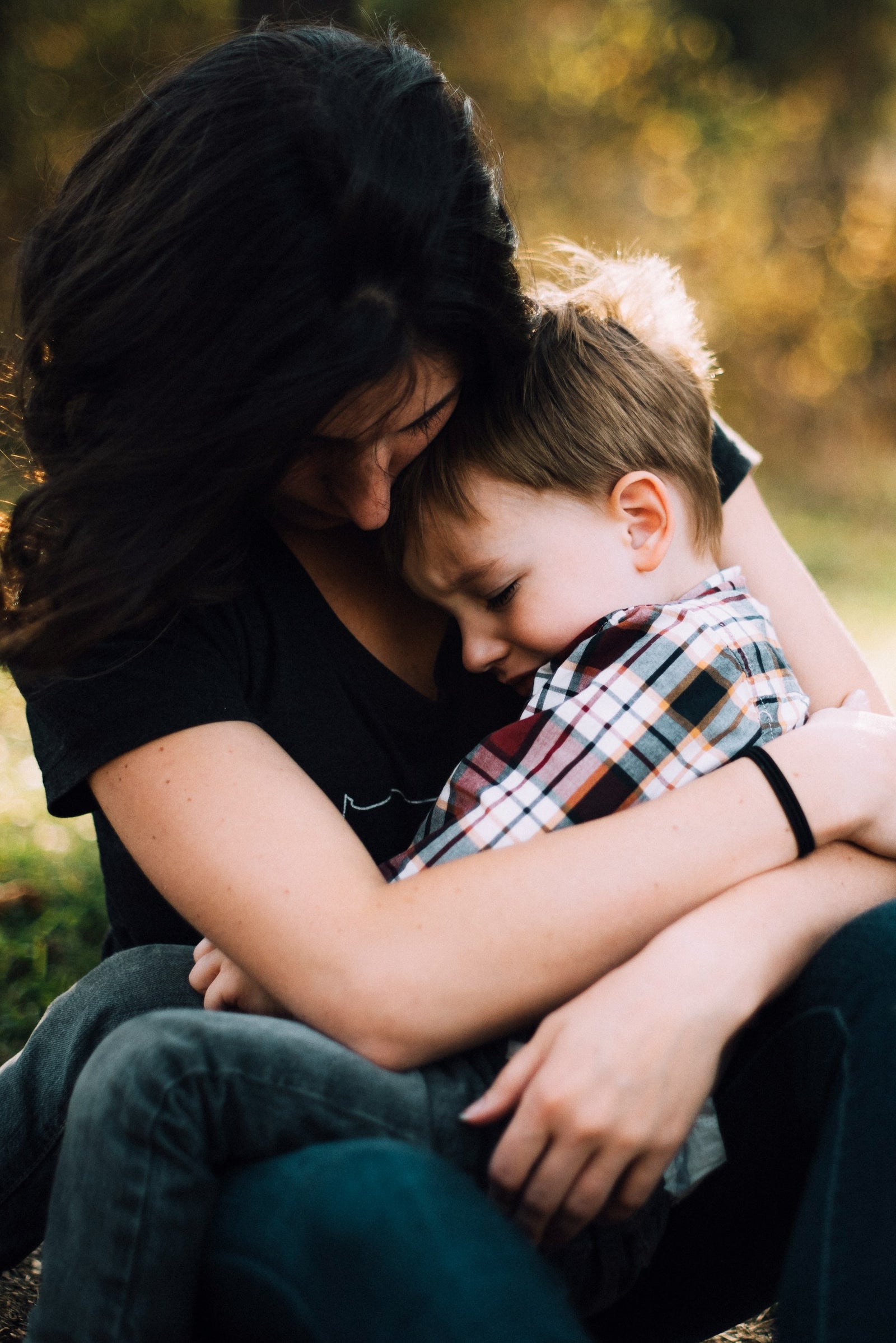 photo of a woman with black hair wearing a black t-shirt cradling a small boy in her arms