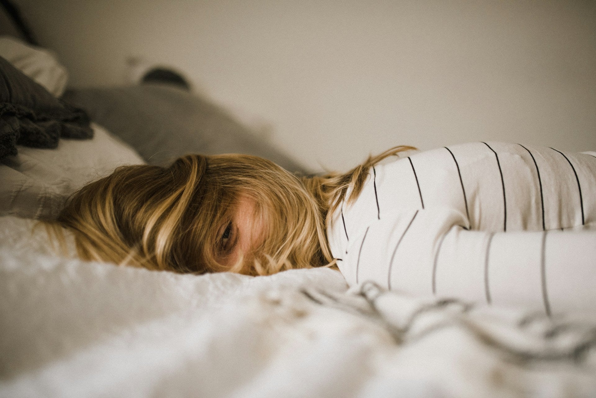 photo of a blonde woman wearing a white shirt with thin black stripes laying on her stomach with her hair covering her face