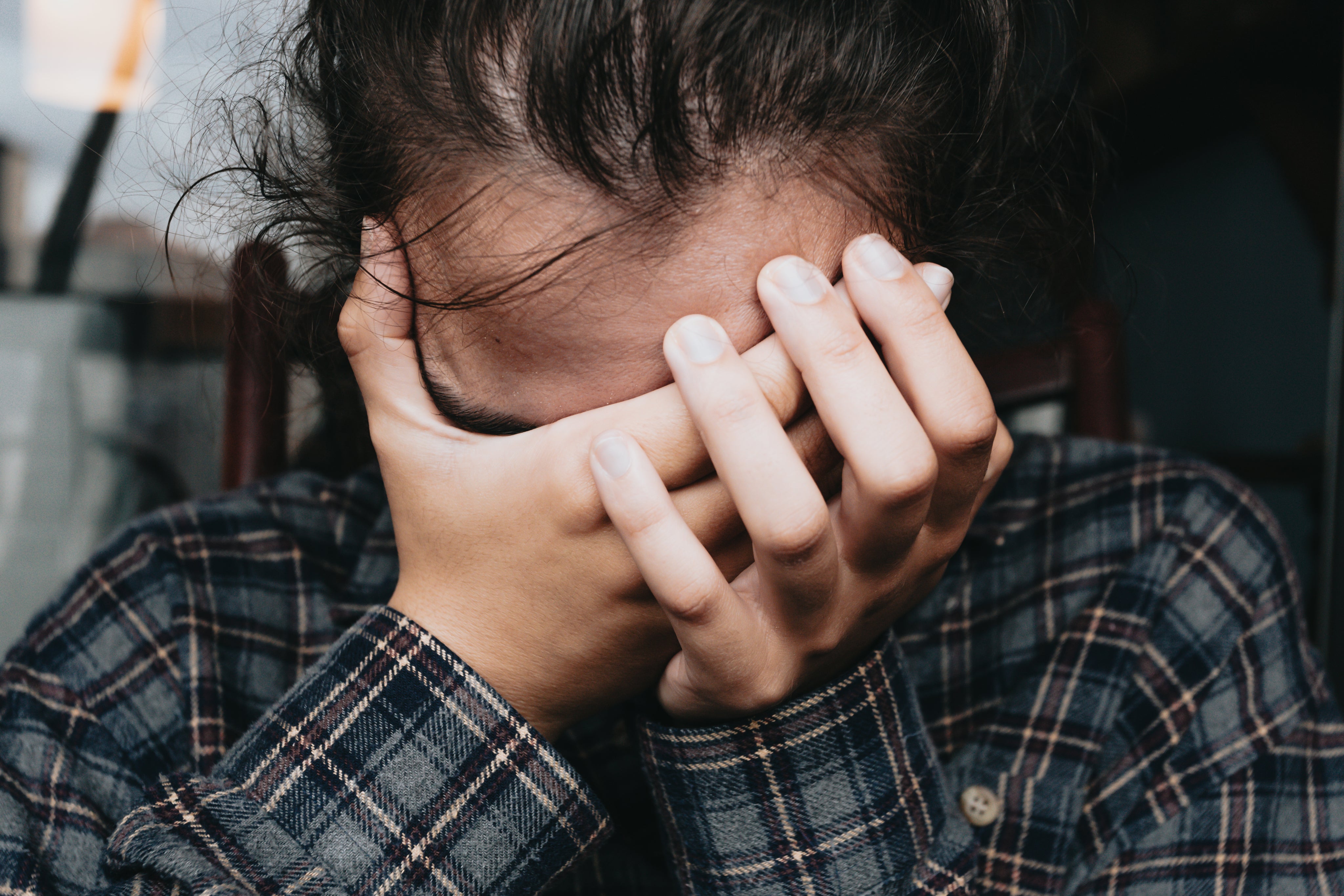 photo of a woman with dark hair and a blue flannel shirt holding both her hands over her eyes