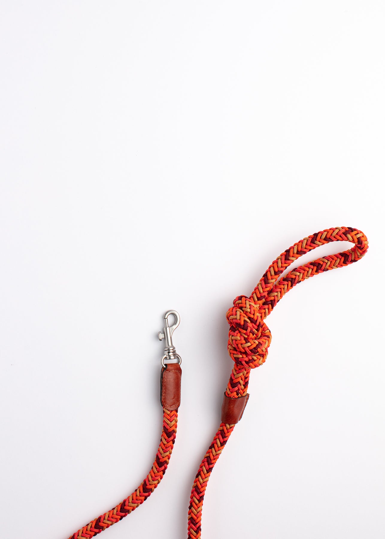 A braided bright orange pet leash with a silver clasp sitting on a flat, white surface