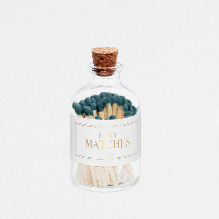 A glass container with a white label including Fancy Matches text filled with green matches against a white background